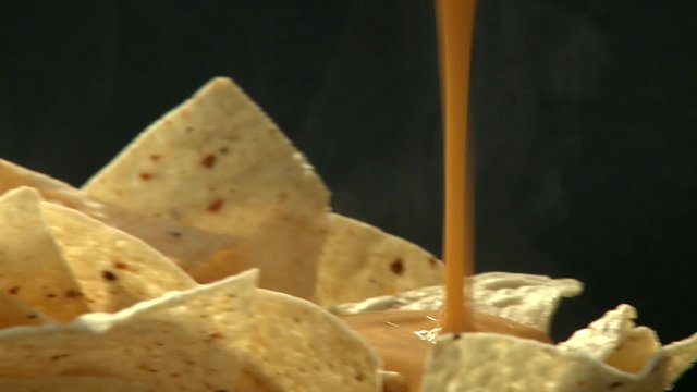 Pouring cheese dip over tortilla chips