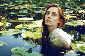 Tender young woman swimming in the pond among water lilies