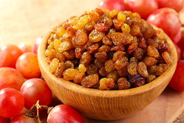 Raisins in bowl with grapes on table close up