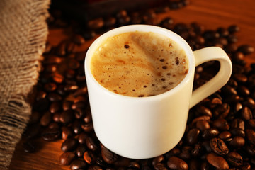 Cup of fresh coffee with beans on table, closeup