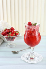 Strawberry dessert with ice in glass, on wooden table, on light background