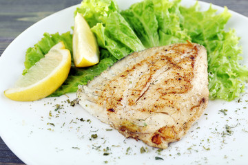 Dish of fish fillet with lettuce and lemon on table close up