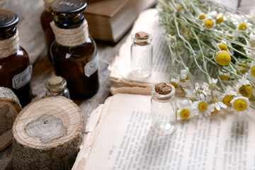 Old book with dry flowers and bottles on table close up