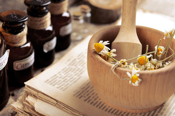 Old book with dry flowers in mortar and bottles on table close up
