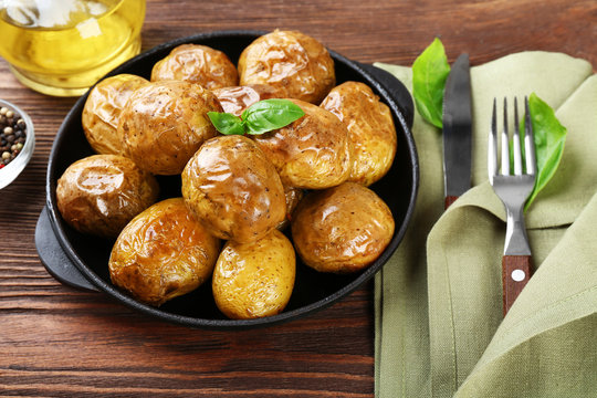 Baked potatoes in pan on wooden table, closeup