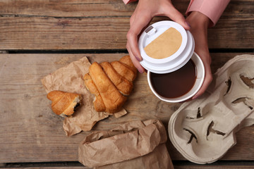 Female hands holding cup of coffee and cookies on wooden table close up