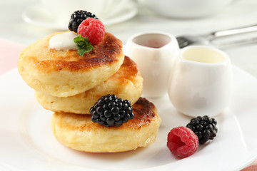 Fritters of cottage cheese with berries in plate on table, closeup