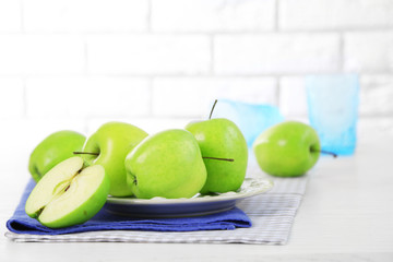Green apples in plate on table with napkin on white brick wall background