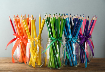 Bright pencils in glass jars on wooden table, on grey background