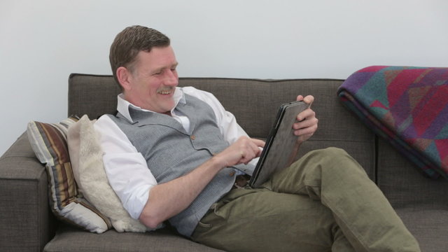 man sitting on couch and writing on his tablet 