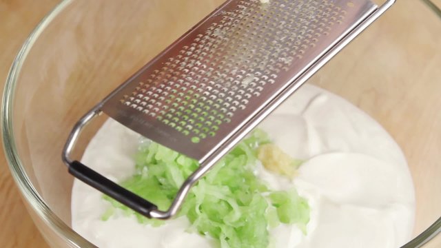 Yogurt and cucumber being seasoned with garlic and pepper