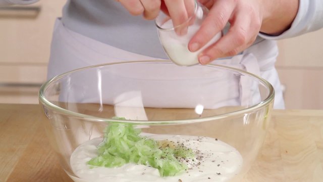 Yogurt and cucumber being seasoned with salt and drizzled with olive oil