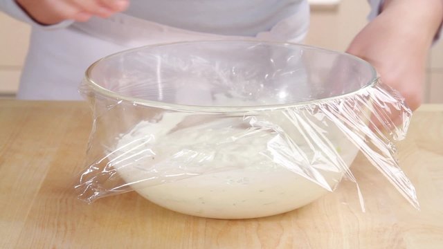 Tzatziki in a glass bowl being covered with cling film