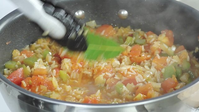 A simmering rice and vegetable stew being seasoned with salt and ground black pepper
