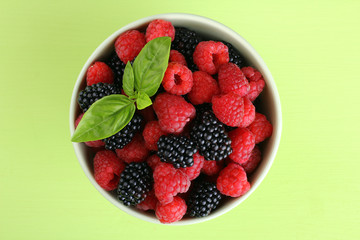 raspberries and blackberries in a bowl of light green background