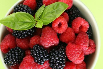 raspberries and blackberries in a bowl of light green background