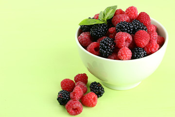 raspberries and blackberries in a bowl of light green background