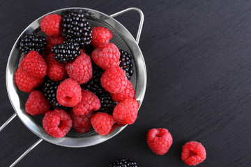 raspberries and blackberries in a bowl black background