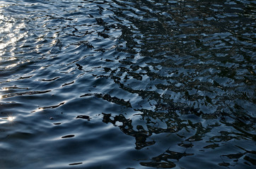 Dark blue ripples on the dark black water's surface at twilight