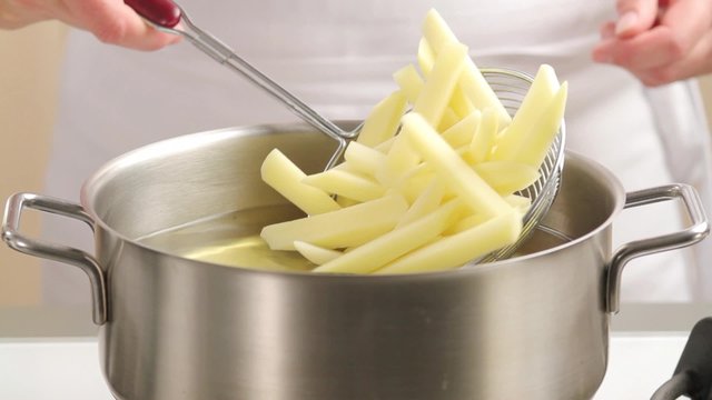 Placing chips in the deep-frying fat using a slotted spoon