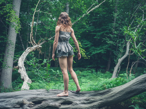 Barefoot woman standing on a fallen tree in the forest