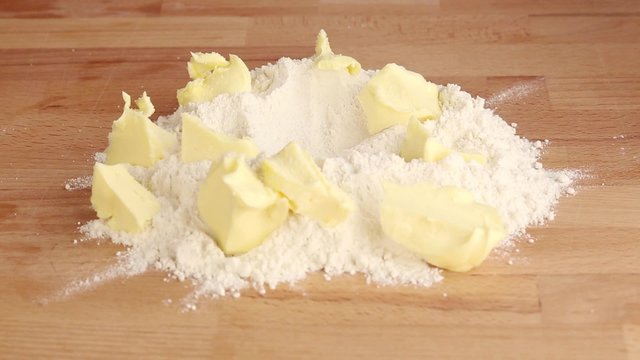 Chopped butter on a pile of flour being sprinkled with salt