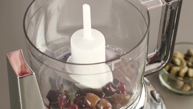 Olives, capers and sardine fillets being placed in a blender