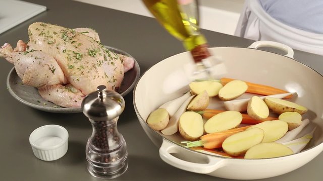 Vegetables being drizzled with oil, seasoned and placed around a chicken