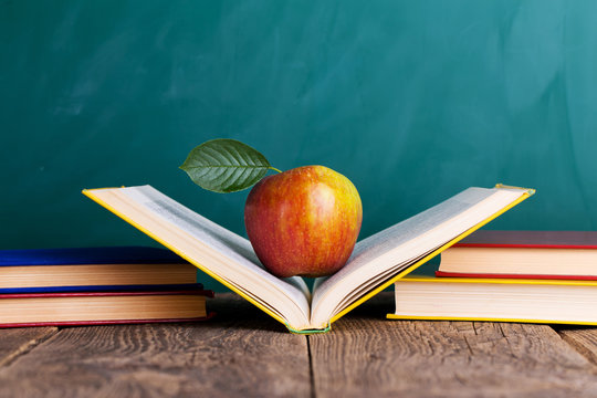 Still life with school books and apple against blackboard with "