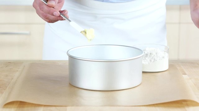 A baking tin being spread with butter and dusted with flour