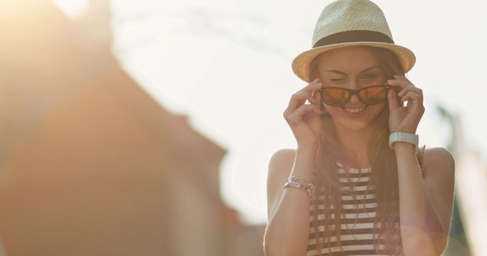 Beautiful Young Woman smiling in the European city, cinematic portrait. Slow Motion, 4K. Happy Hipster girl enjoying the sun and the life. Travel in style. Lens flare. 