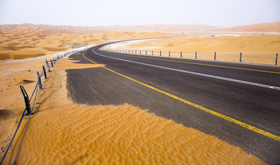 Winding black asphalt road through the sand dunes of Liwa oasis, United Arab Emirates