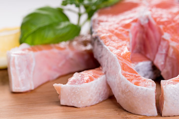 Close up on raw steak of salmon with herbs on wooden cutting board.