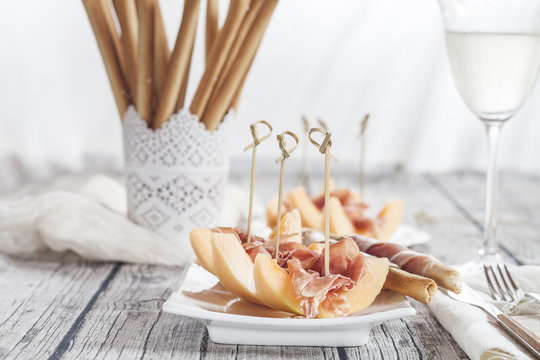 Plate of Charentais melon slices with ham and Grissini wrapped with ham