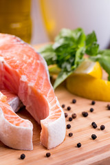 Close up on raw steak of salmon with lemon and herbs on wooden cutting board.