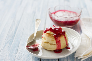 Freshly baked homemade scone with raspberry jam on a white plate, selective focus