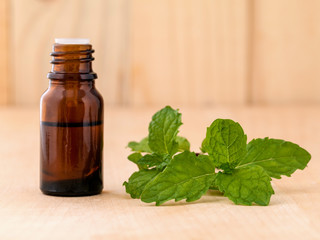 Bottle of mint essential oil on wooden background with selective