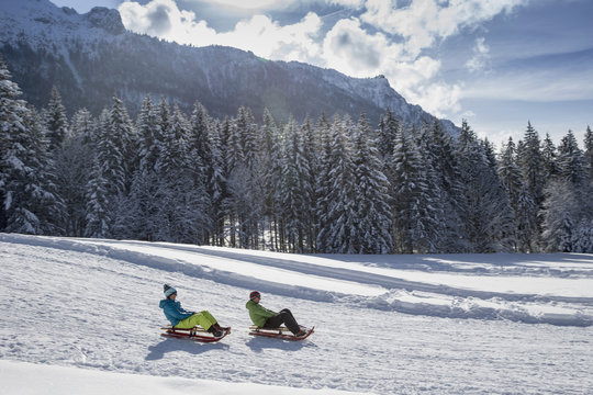 Germany, Bavaria, Inzell, couple on sledges in snow-covered landscape