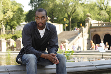 Obraz premium Man with clasped hands sitting on edge of fountain.