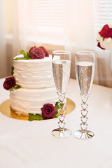 beautiful white cake with red roses and two glasses with champagne