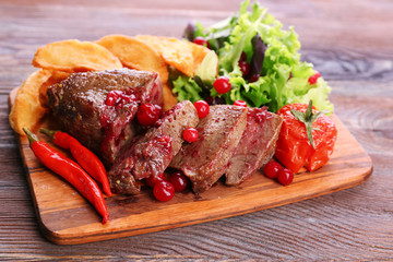 Beef with cranberry sauce, roasted potato slices on cutting board, on wooden background