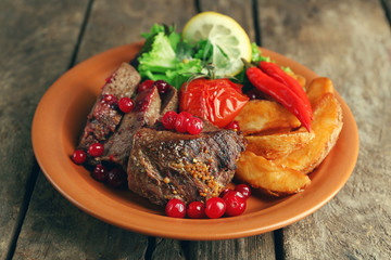Tasty roasted meat with cranberry sauce, salad and roasted vegetables on plate, on wooden background