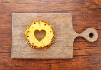 Pineapple slice with cut in shape of heart on wooden background