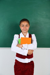 Beautiful little girl standing near blackboard in classroom