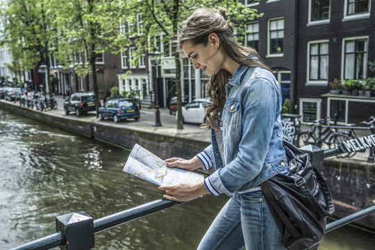 Netherlands, Amsterdam, female tourist looking at city map in front of town canal