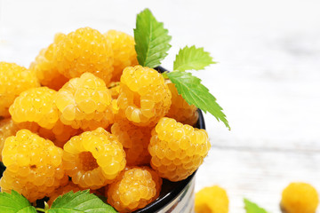 Cup of yellow raspberries on wooden table, closeup