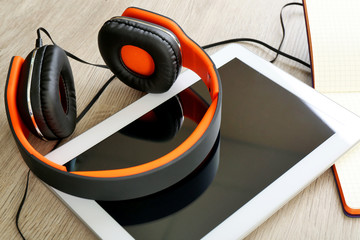 Headphones with tablet and notebook on wooden table close up