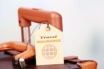 Suitcase with TRAVEL INSURANCE label on light blurred background