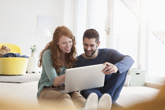 Smiling young couple sitting on floor in the living room using laptop
