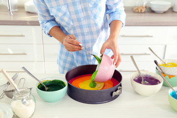 Young woman making rainbow cake in kitchen